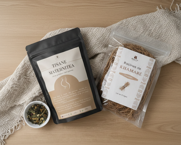 Vue de dessus d'un pack bien-être composé d'un sachet de "Tisane Maternitea" noir et d'un sachet transparent de "Racines de Khamaré", disposés sur une table en bois clair avec un linge en coton beige et un petit bol de plantes séchées.